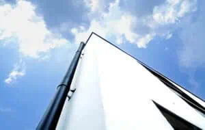 Modern minimalist home facade with white stucco wall and black drainpipe under bright blue sky.