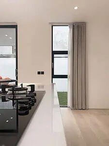 An island kitchen with stove on top and a view to the garden through black frame windows