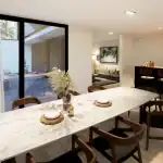 3D render of the dining room of villa NS with white marble dining table, modern hardwood chairs and view to the black kitchen island