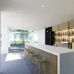 3D render of the outdoor bar area of villa TV with light wood cladded bar, white countertop and numerous bottles stored on the shelves in the back