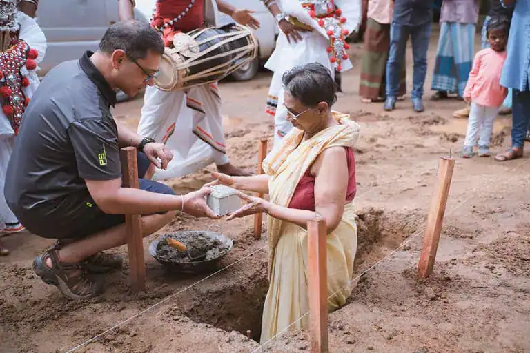 Client placing the first stone at a foundation-laying ceremony, surrounded by traditional dancers and MVIVO staff