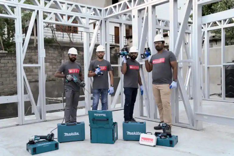MVIVO construction team in hard hats and branded T-shirts holding Makita tools at a light steel frame building site