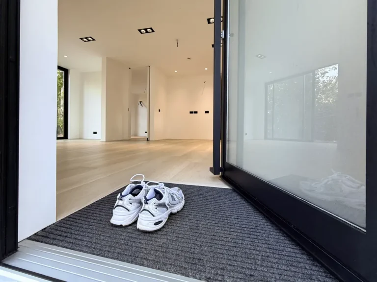 Pair of white sneakers on a carpeted mat at the entrance of a modern minimalist home