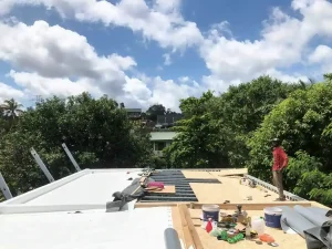Workers installing a flat roof system under clear blue skies in Sri Lanka, showing insulation and waterproofing layers.
