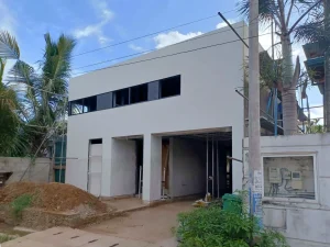 Modern two-storey house under construction with smooth white exterior walls and tropical surroundings.