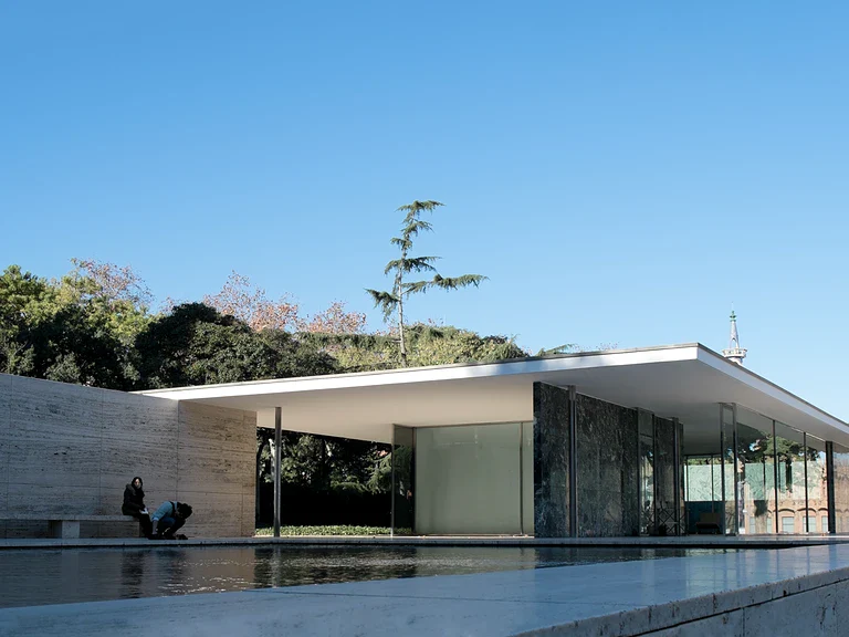 Barcelona Pavilion by Ludwig Mies van der Rohe featuring minimalist modernist design with flat roof, travertine walls, glass panels, and reflecting pool under a clear blue sky.