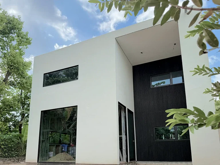 A modern two storey villa in Sri Lanka with a white exterior, black cladding and wide horizontal windows framed by trees.